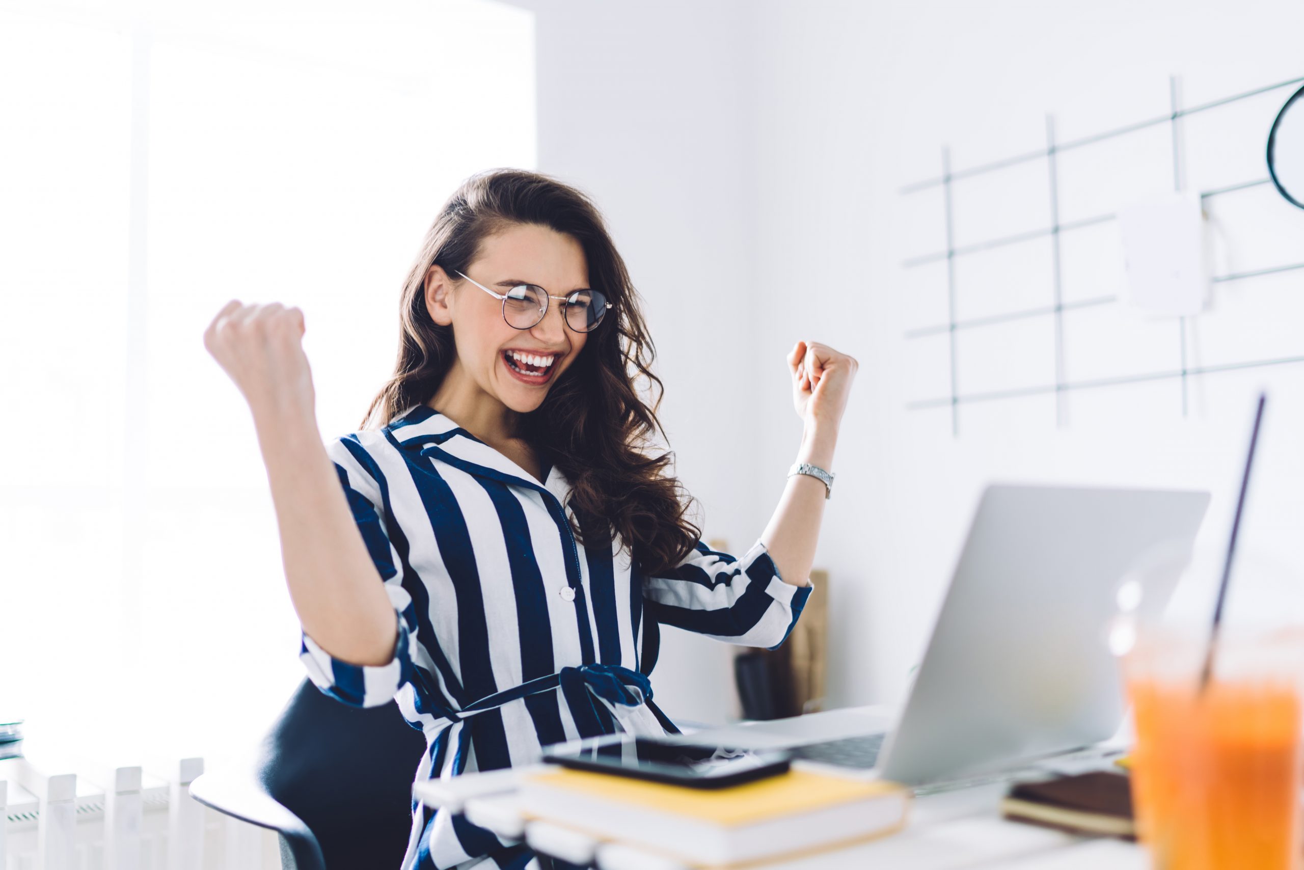 Happy young woman sitting at table with hands up in winner gesture Locking down a new role during COVID