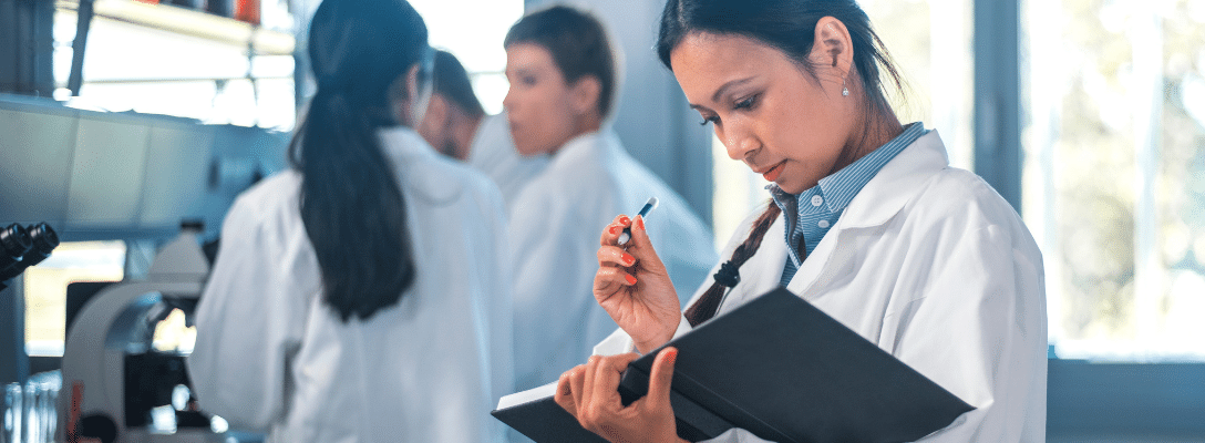 Intapeople Gender Stem header image females in lab coats one in foreground about to write results