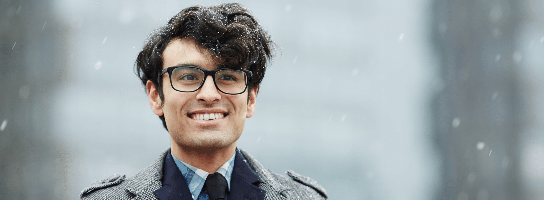 Employee wellbeing in winter blog header man wearing glasses in a shirt and overcoat in snow employee winter