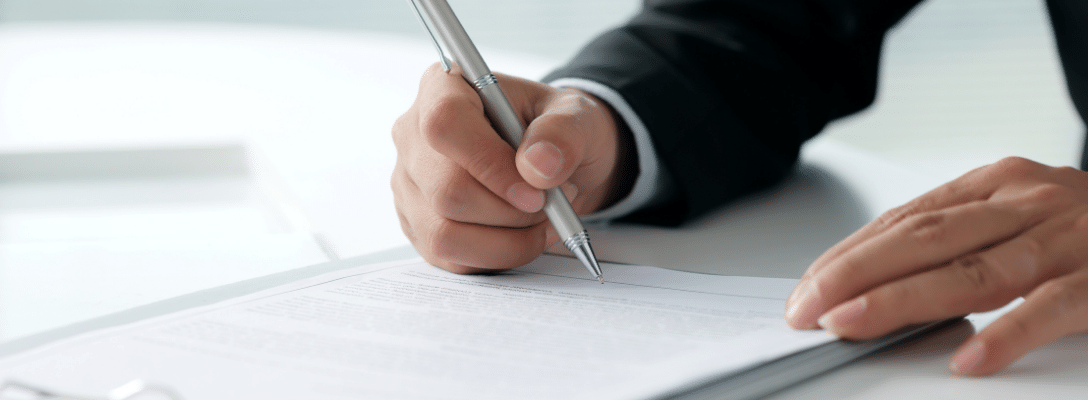 person in suit writing on contract on white desk