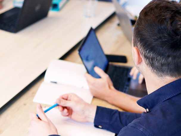 Looking over the should of a person at a notebook and laptop on a desk