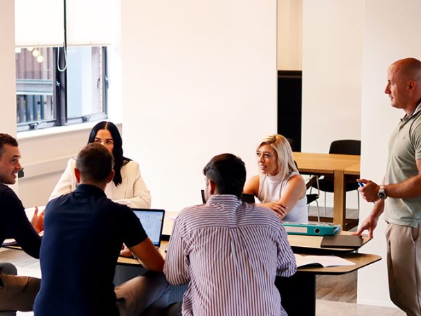 Group of people sat working around a desk with one person standing