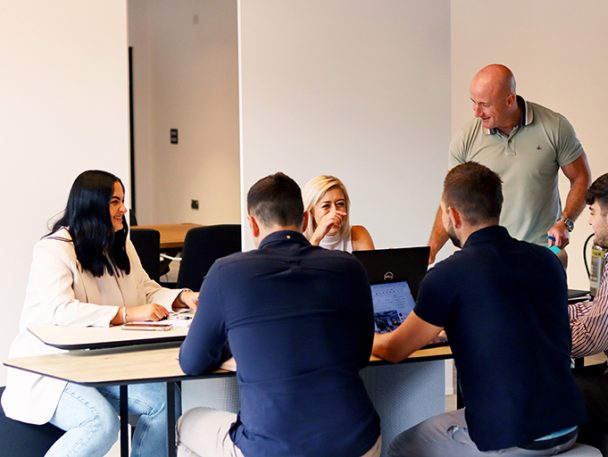 Group of people sat working around a desk with one person standing