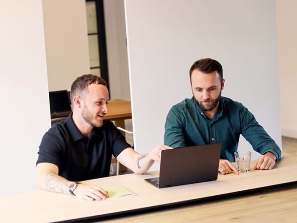 Two men sat at a desk working on a laptop together